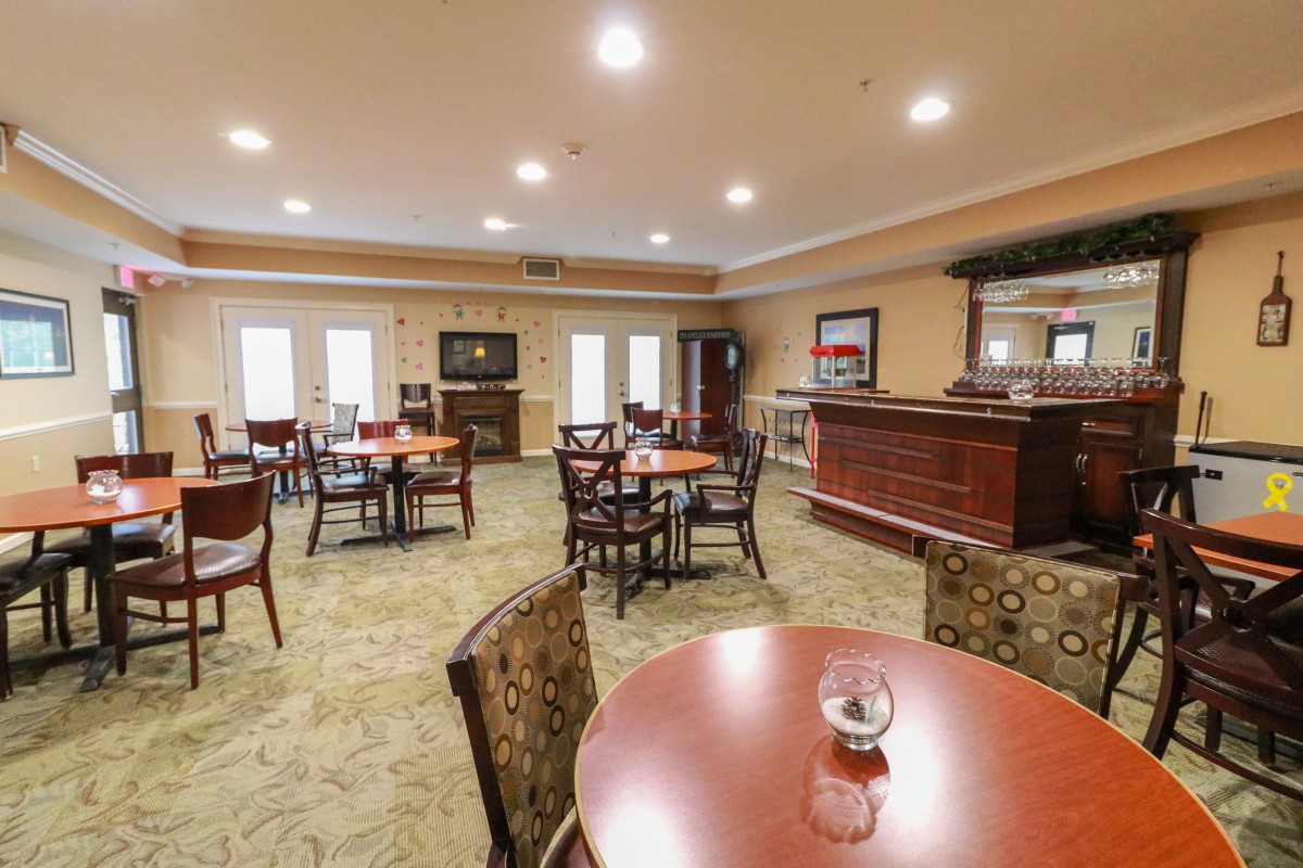 A cozy dining area with wooden tables and upholstered chairs, well-lit and carpeted.