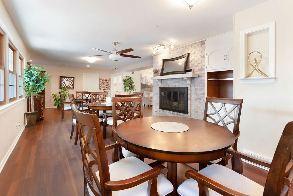 A modern dining room featuring a round wooden table, cushioned chairs, and a fireplace with a white stone finish.