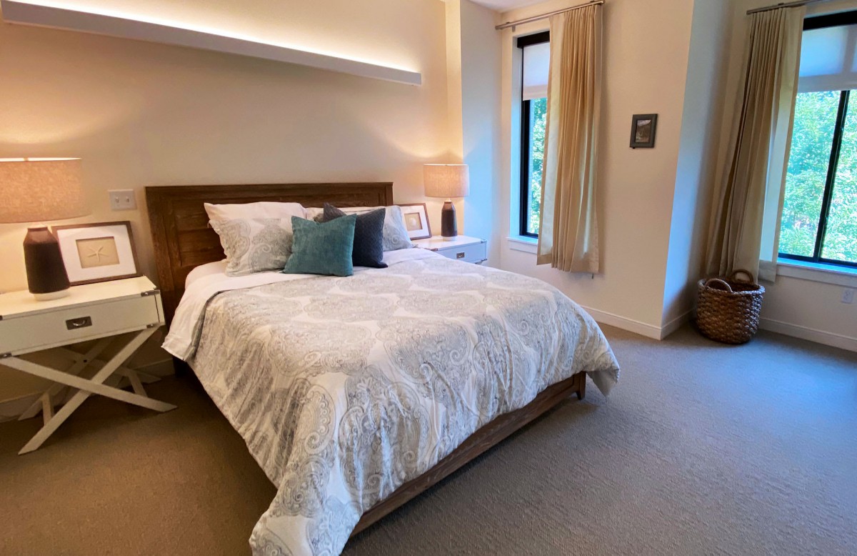A cozy bedroom featuring a neatly made bed with decorative pillows, a bedside lamp, and a window with curtains.