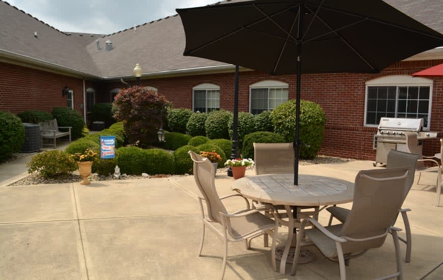 A tranquil patio area with outdoor seating and an umbrella, surrounded by well-maintained gardens and a brick building.