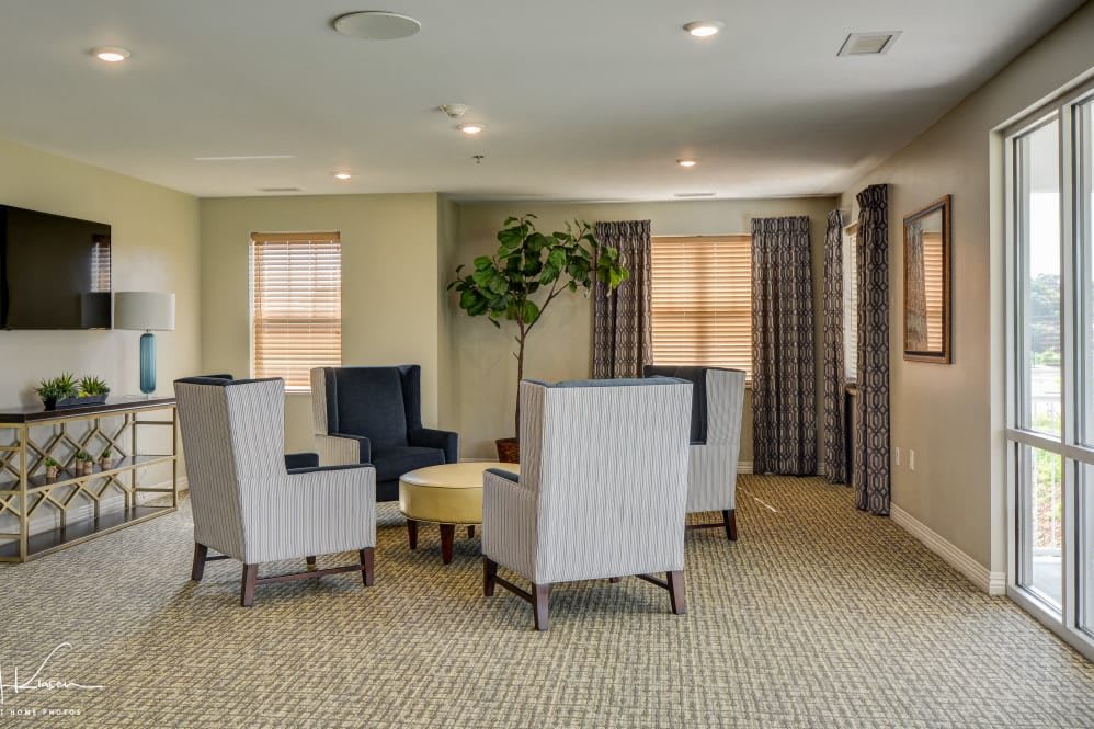 A cozy living room with comfortable chairs grouped around a small round table, featuring natural light and decorative curtains.