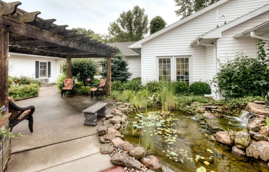 A serene backyard featuring a pond, lush landscaping, and a pergola with cozy seating.