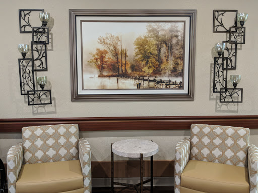 A cozy seating area featuring soft chairs, a small table, and a nature-themed painting.