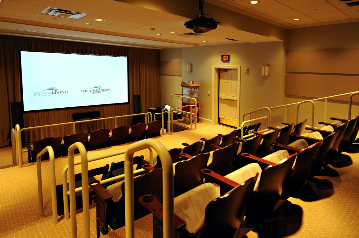An empty lecture hall with a projector screen and seating.