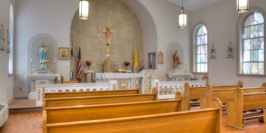Interior of a church showcasing wooden pews and the altar with a crucifix.