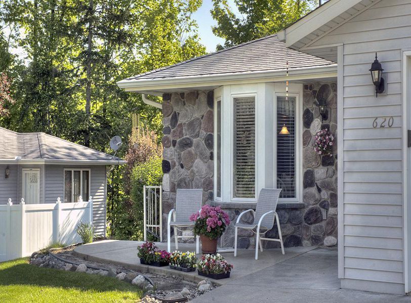A cozy porch with two chairs and vibrant flowers, set against a stone wall.