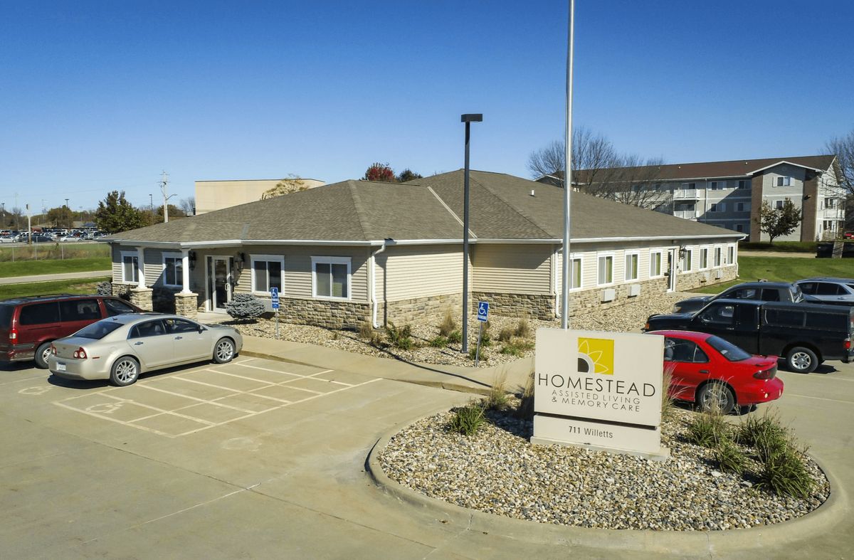 A single-story building with a parking lot and sign in the foreground under a clear blue sky.
