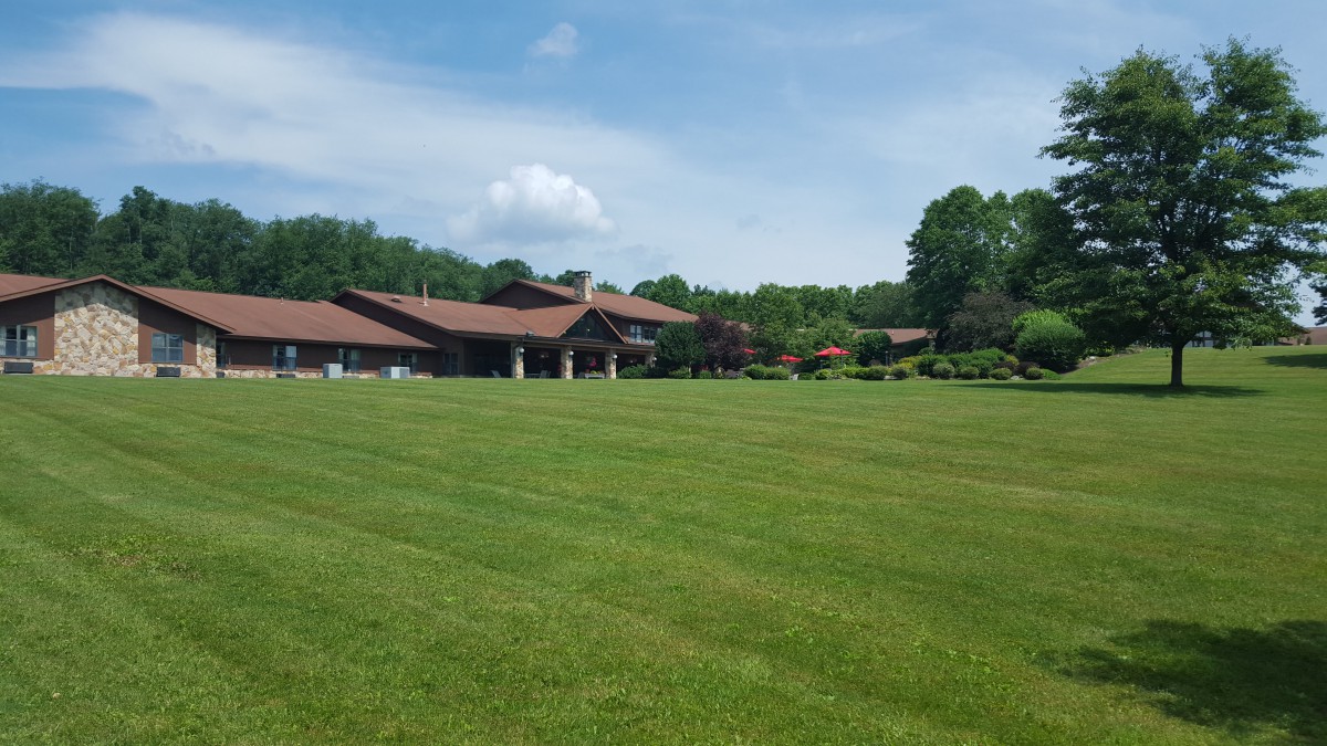 A beautiful house with a large, well-maintained lawn and surrounding greenery under a clear blue sky.