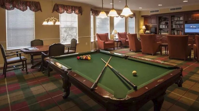 A cozy game room featuring a pool table with cues and balls set up, surrounded by comfortable seating and soft lighting.