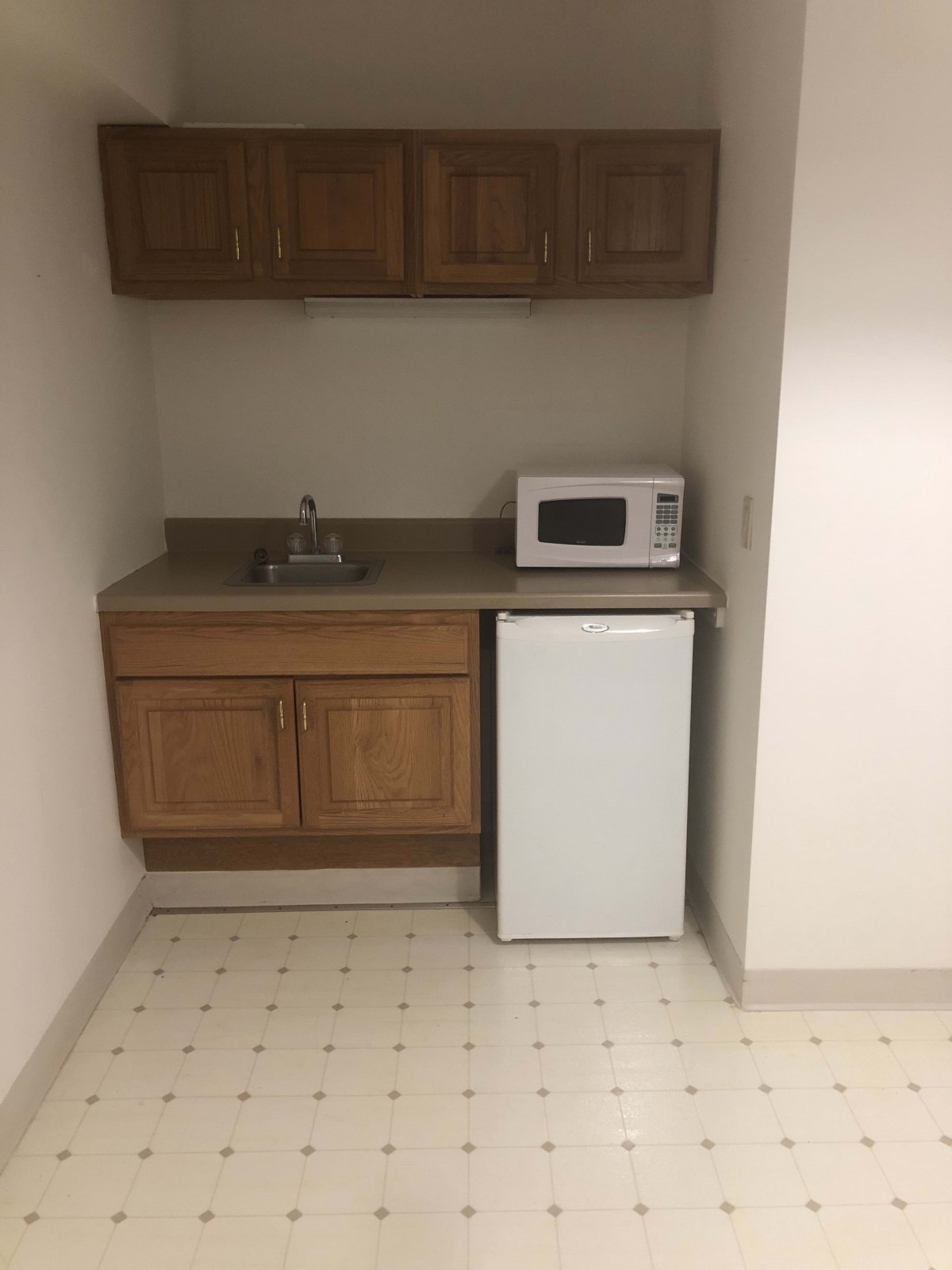 A small kitchenette with a microwave, mini fridge, sink, and wooden cabinets.