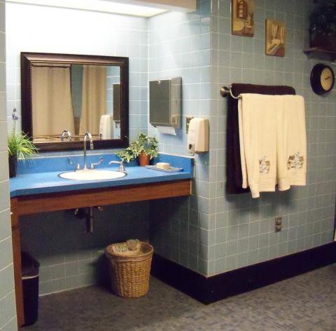 A vintage-style bathroom with blue tiles, featuring a sink, mirror, and neatly hung towels.