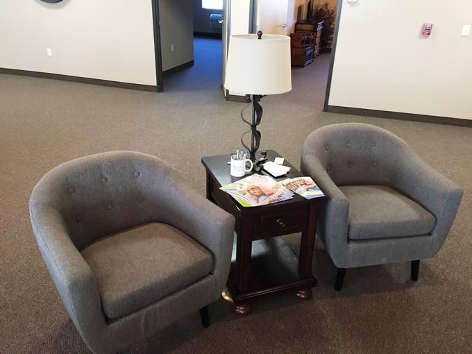 A cozy waiting area with two gray chairs, a small table, and a lamp.