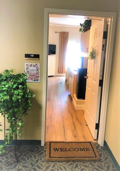 A hallway view leading into a warmly lit room with a decorative plant beside the entrance.