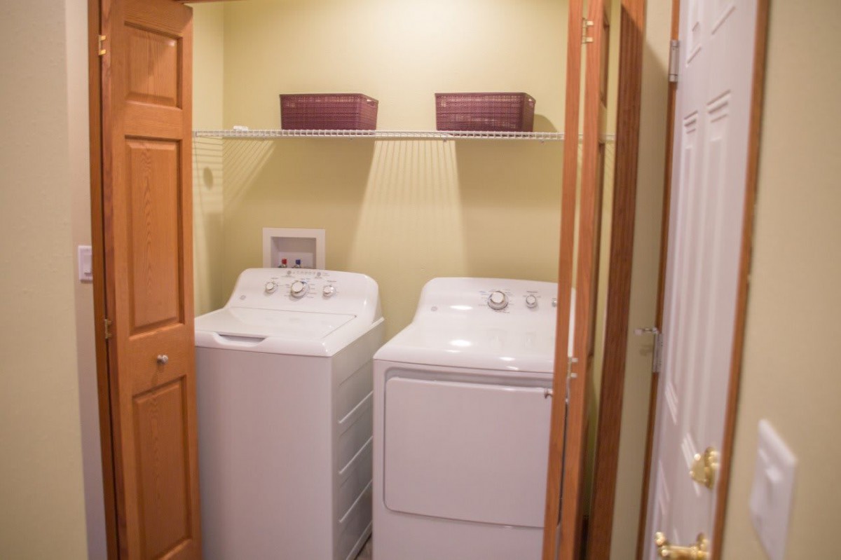 A compact laundry room featuring a washer and dryer set with baskets on an overhead shelf.