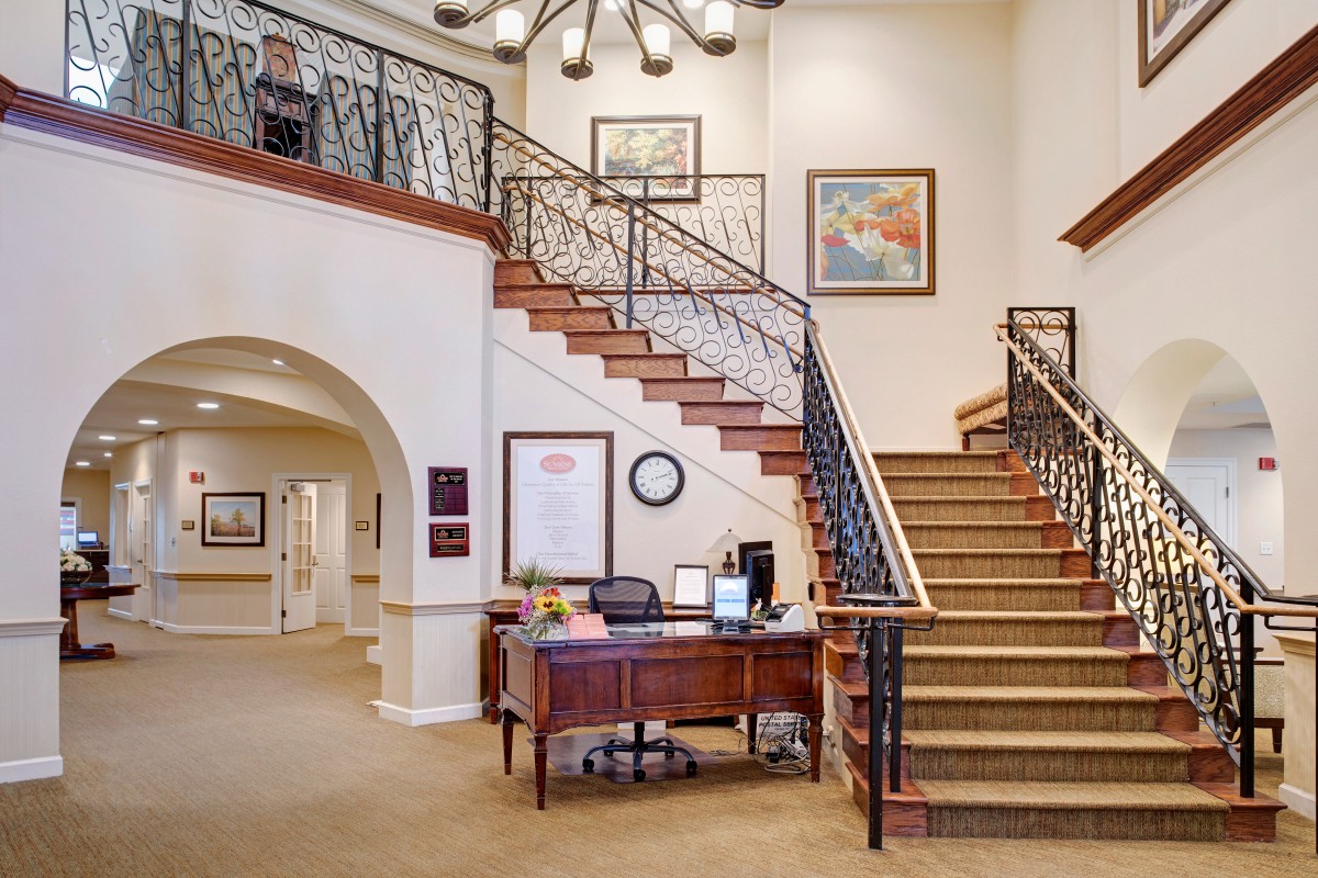 A well-lit lobby featuring a grand staircase with decorative railing and a reception desk.