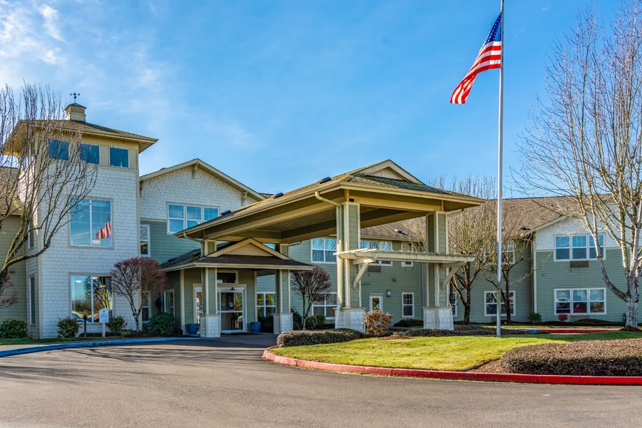 A large building with a covered entrance and an American flag in front on a clear day.