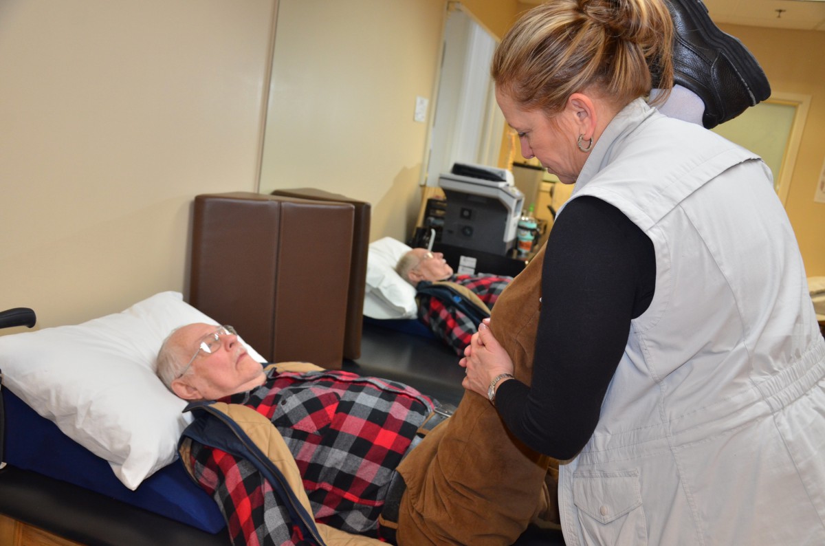 A caregiver assists an elderly man during a therapy session.