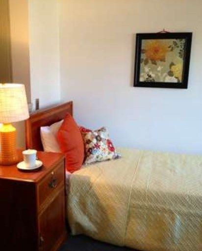 A cozy bedroom with a neatly made bed, decorated with pillows and a bedside lamp on a wooden nightstand.