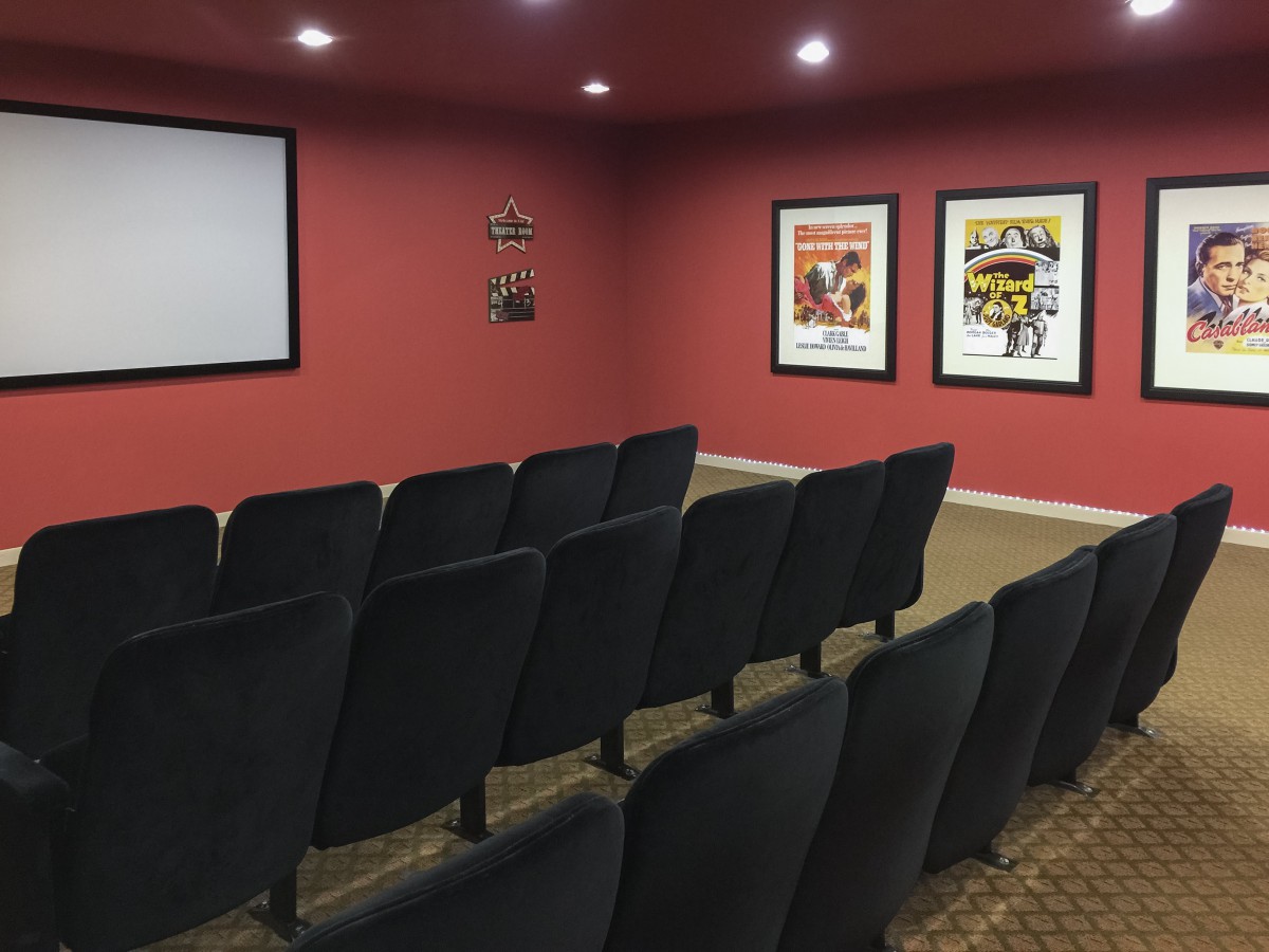 A cozy home theater setup with rows of seats facing a projector screen, adorned with movie posters on red-painted walls.