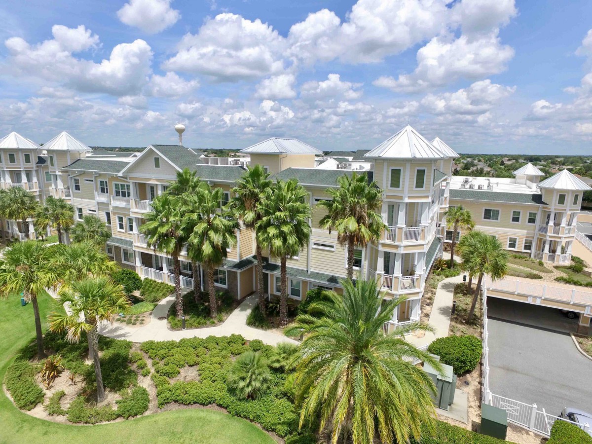A scenic view of a beautiful building surrounded by palm trees and vibrant greenery under a bright blue sky with fluffy clouds.