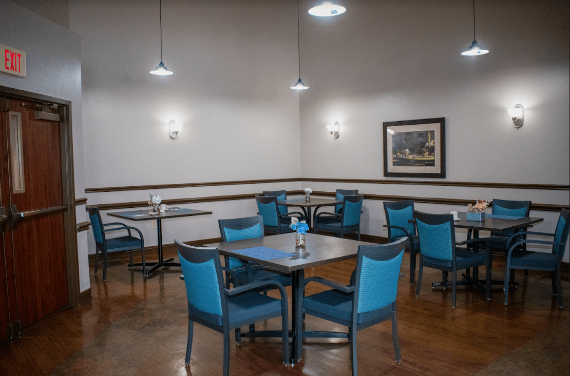 An empty dining area with blue chairs and tables, illuminated by ceiling lights.
