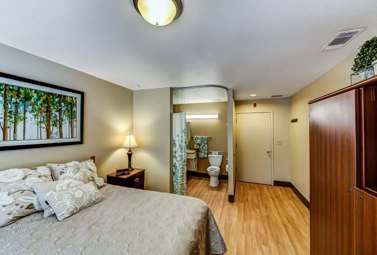A cozy bedroom with a bed, lamp, and visible bathroom area.