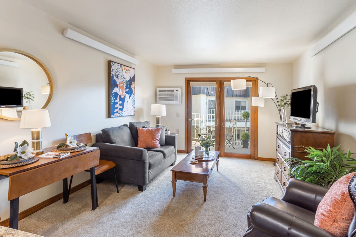 A cozy living room featuring a sofa, coffee table, and artwork on the wall with abundant natural light from large windows.