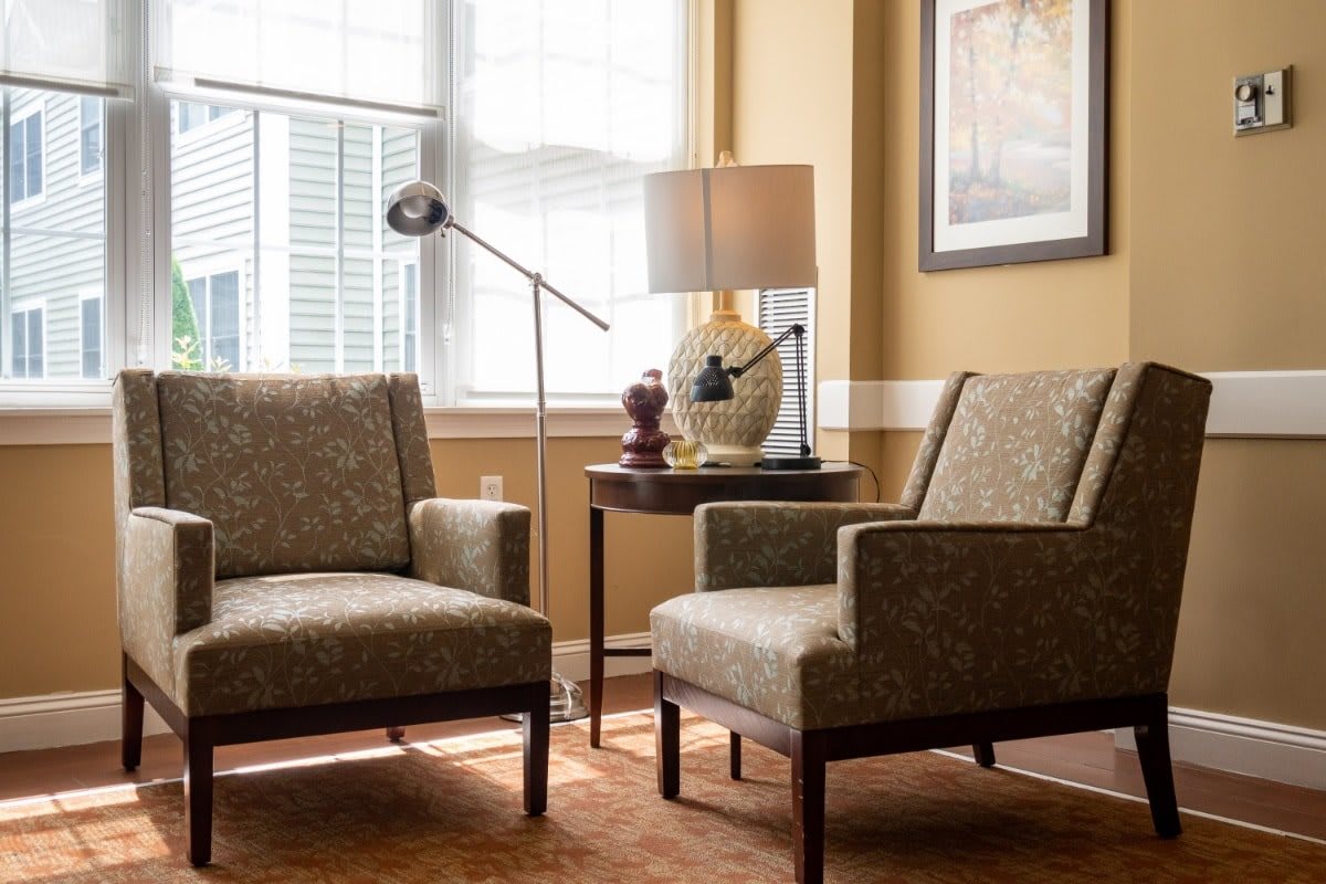 A cozy living room setup featuring two armchairs, a side table with a lamp, and a window allowing natural light to brighten the space.