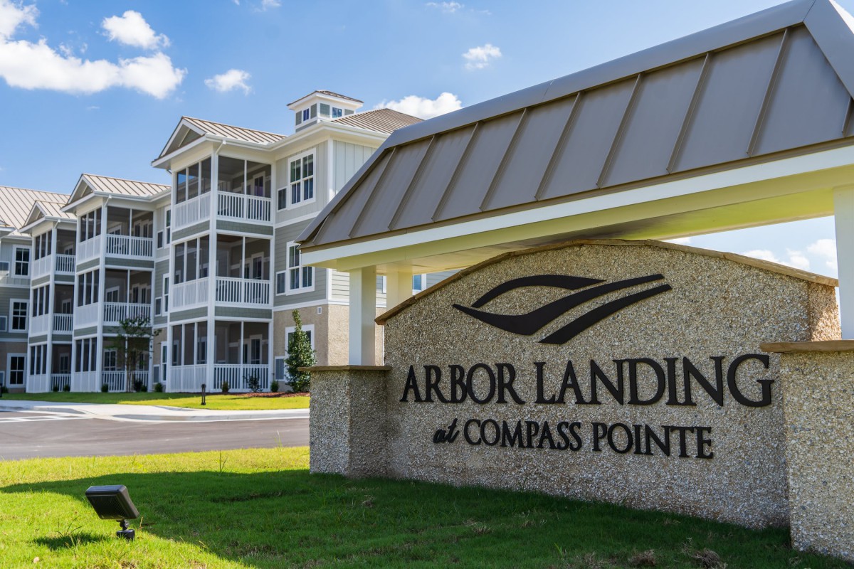 Entrance sign for Arbor Landing at Compass Pointe with a view of residential buildings in the background.