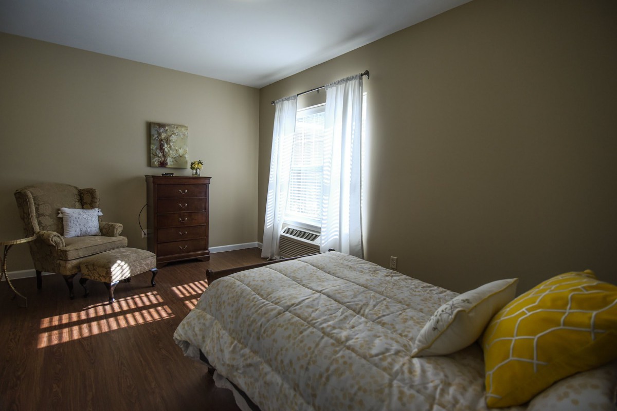 A cozy bedroom with a bed, dresser, and natural light streaming through the window.