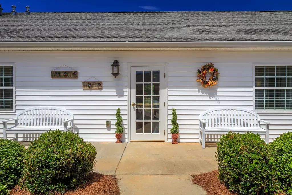 Front view of a house entrance with white siding, decorated with a wreath and flanked by benches.