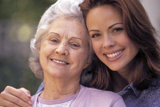 A grandmother and granddaughter smiling together outdoors.