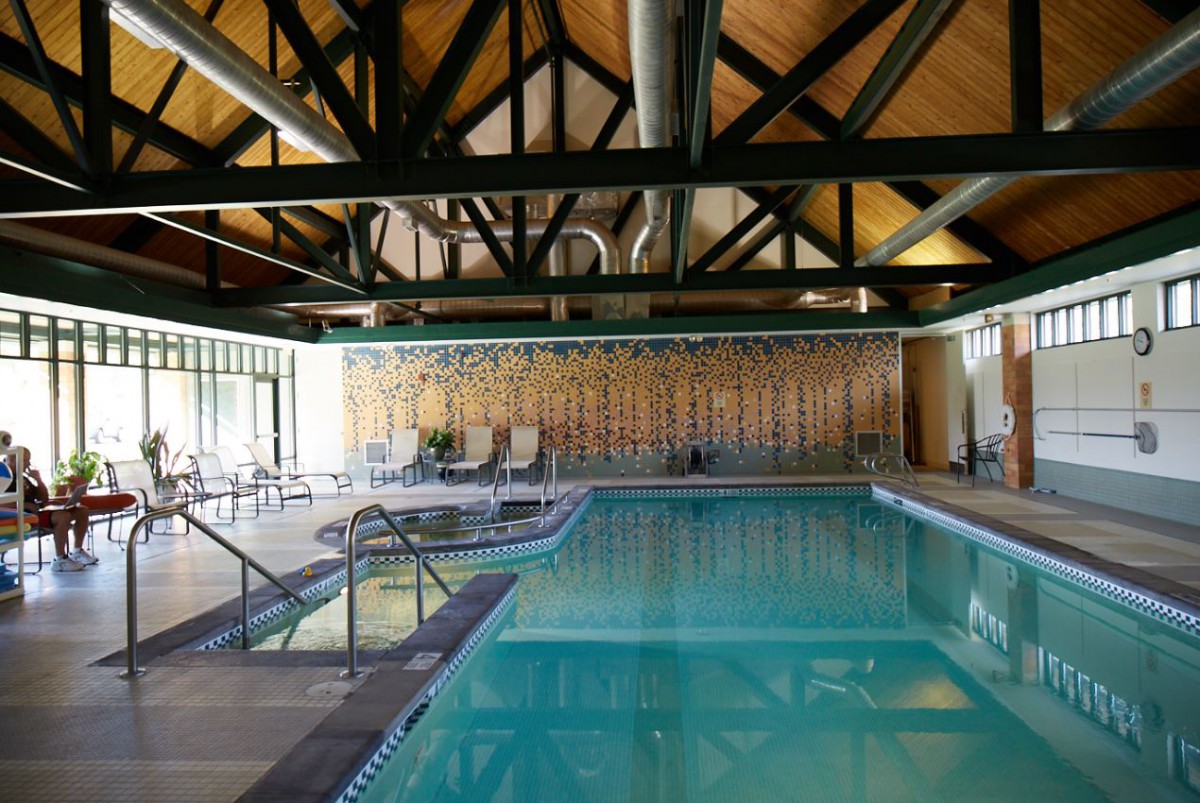 An indoor swimming pool with a wooden ceiling and lounging chairs.