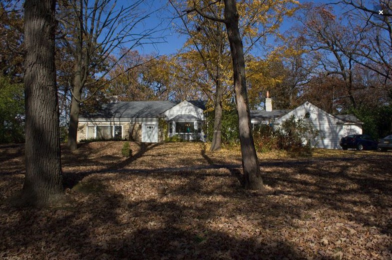 A house surrounded by autumn foliage with fallen leaves on the ground.