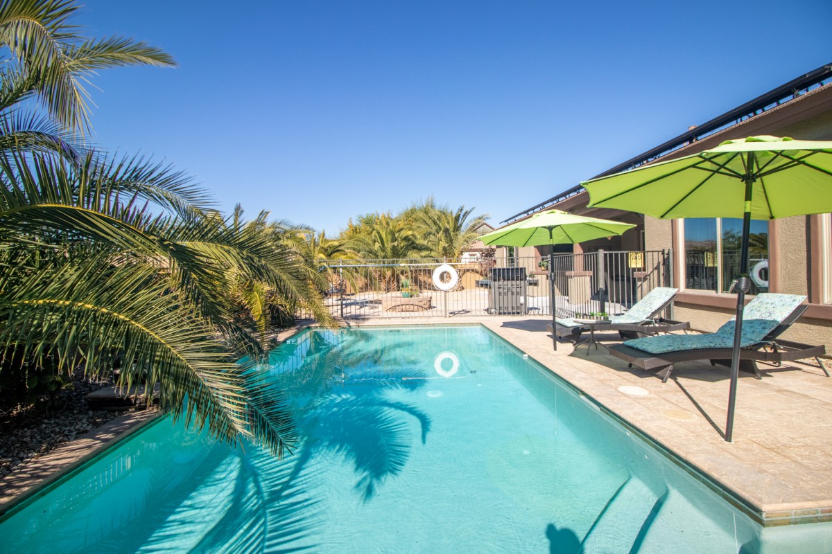 A serene outdoor swimming pool surrounded by palm trees and sun loungers under a clear blue sky.