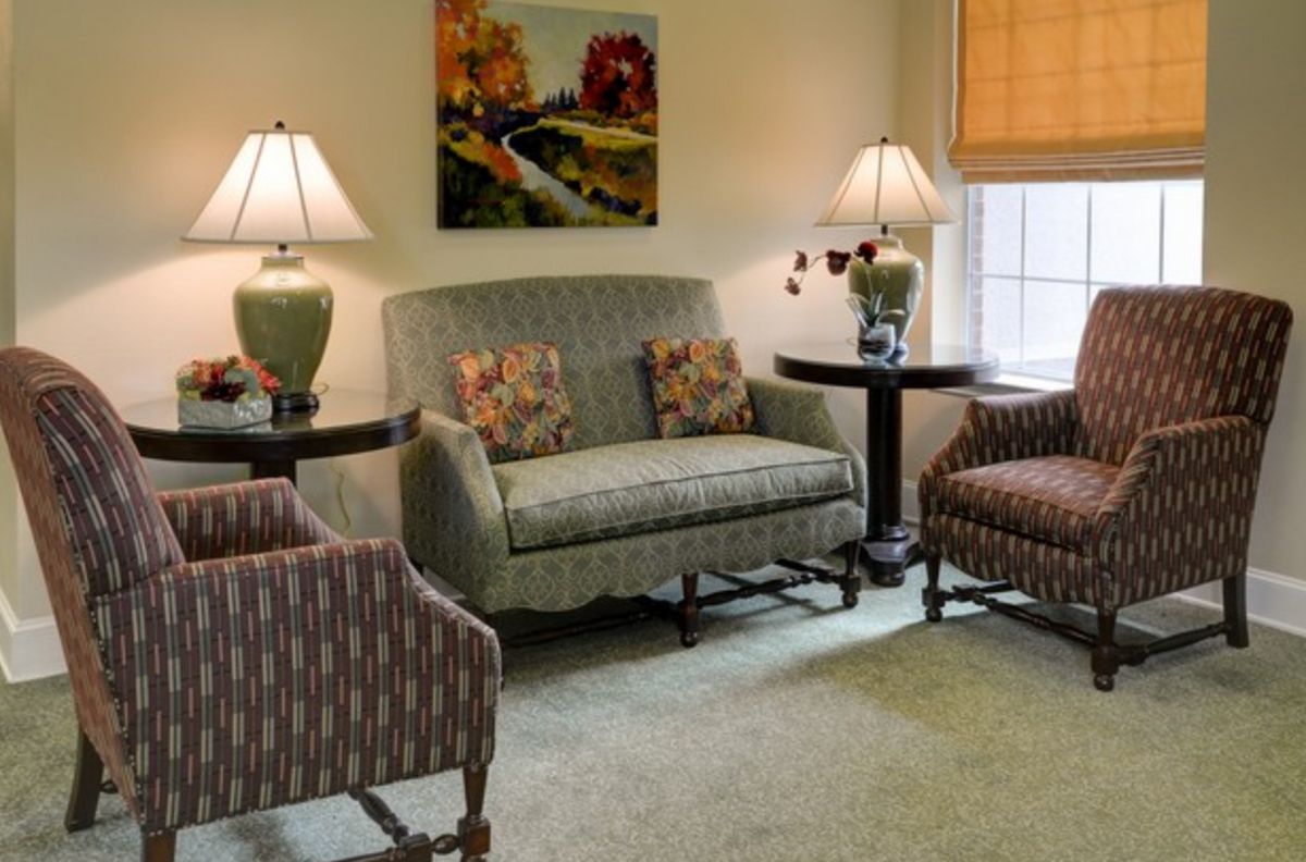A cozy living room with a sofa, two chairs, lamps, and artwork on the wall.