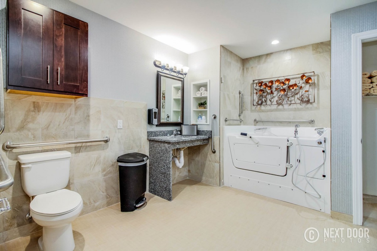 A modern and accessible bathroom featuring a walk-in bathtub, sink with mirror, toilet, and grab bars for safety.