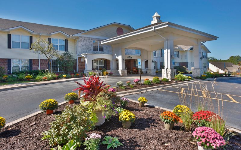 Image of a well-landscaped building entrance with colorful flowers and clear blue sky.