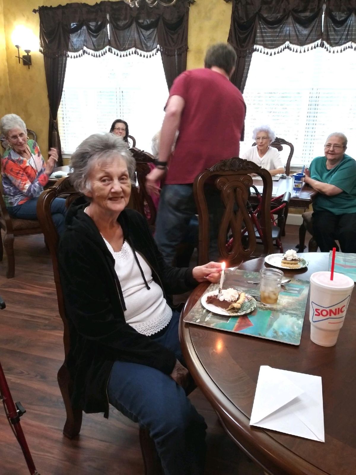 An elderly woman celebrating her birthday with friends, enjoying cake and company indoors.