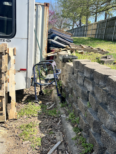 A wheelchair leaning against a concrete wall amidst clutter in a backyard.