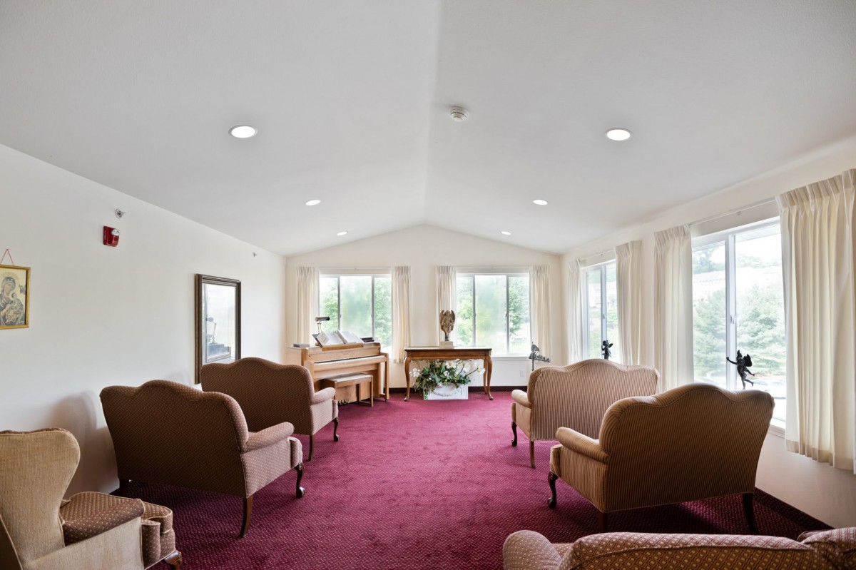 A spacious living room with multiple sofas, a red carpet, and large windows offering natural light.