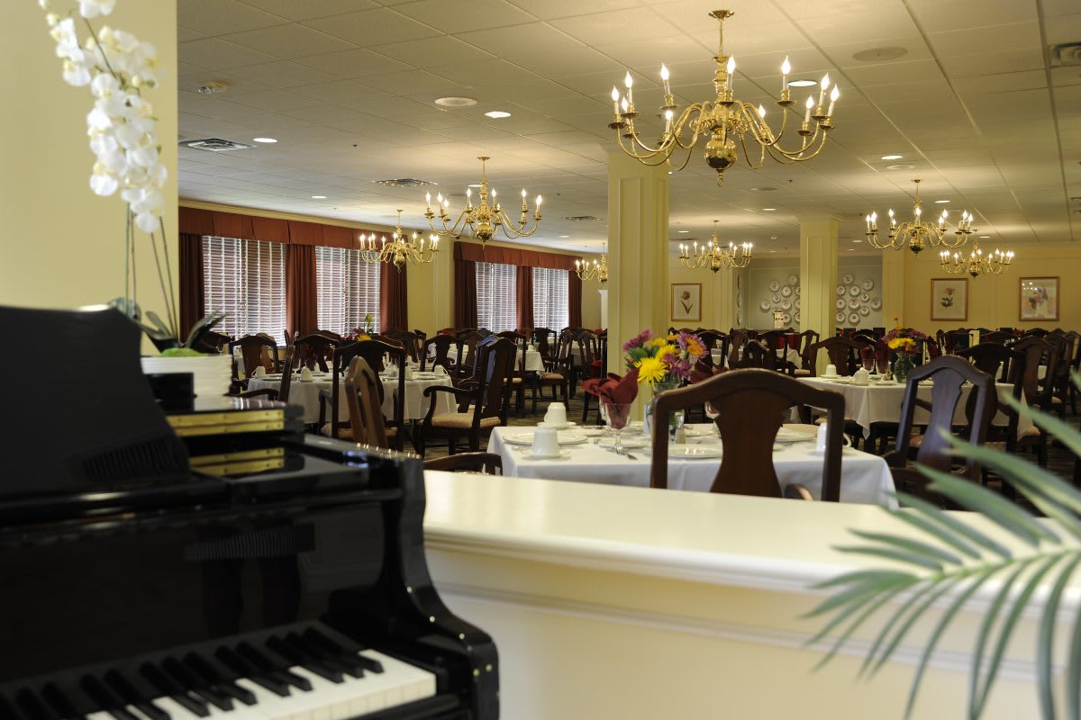 An elegant dining room setting with a black piano and chandeliers.