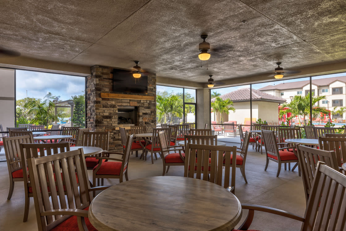 A cozy restaurant interior with wooden tables and chairs, featuring a fireplace and ample natural light from large windows.