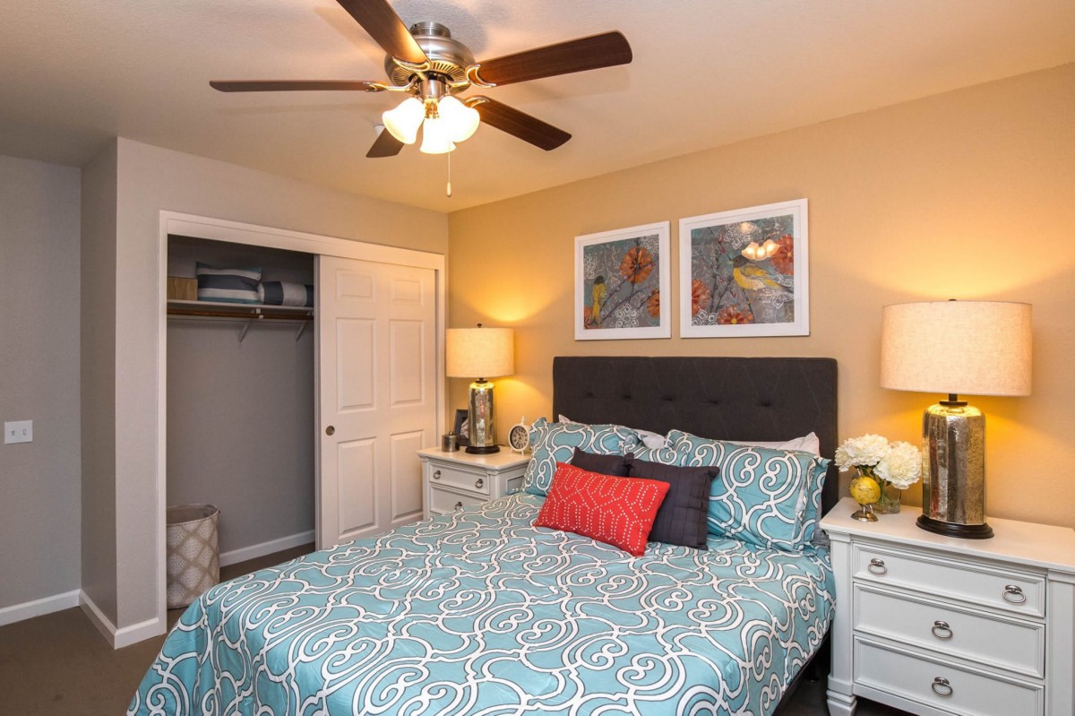 A cozy bedroom with a neatly made bed, accent pillows, and two bedside tables under a ceiling fan.