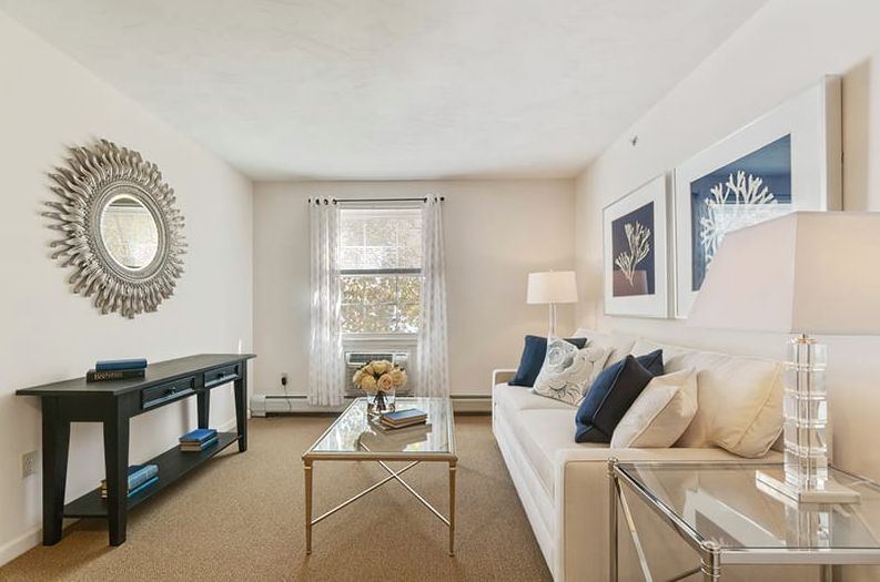 A cozy living room with modern decor, featuring a comfortable sofa, coffee table, artwork on the walls, and a large window allowing natural light in.