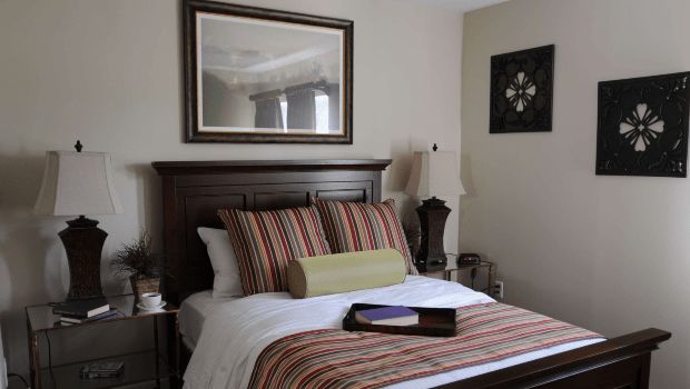 A cozy bedroom with a neatly made bed featuring striped pillows, a decorative mirror above the headboard, and elegant bedside lamps.