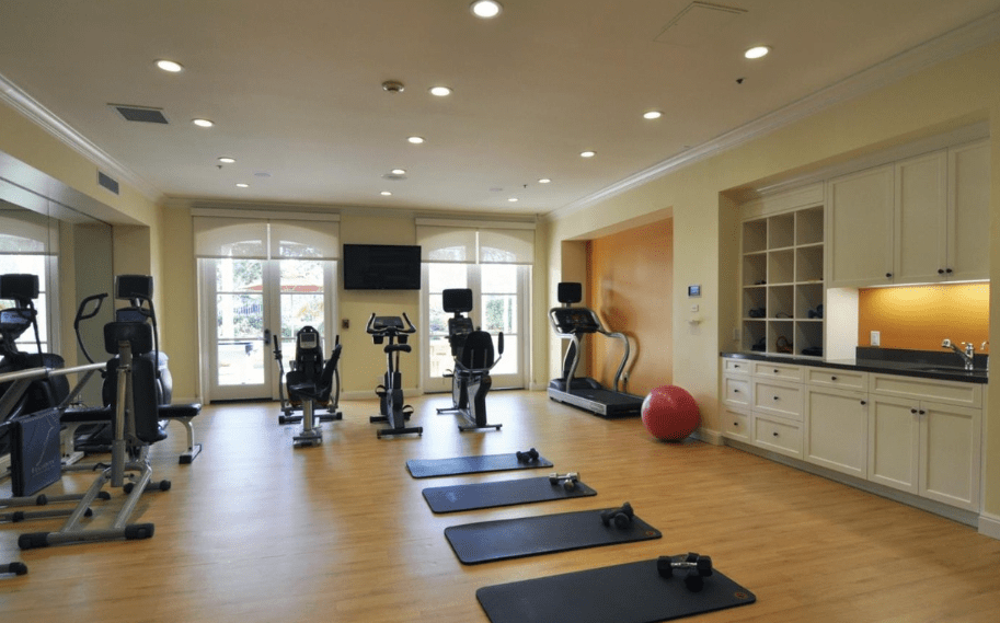 A well-lit gym with various exercise equipment including treadmills, stationary bikes, yoga mats, and an exercise ball.
