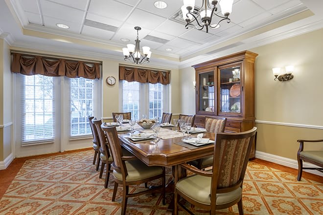 An elegant dining room with a large wooden table, surrounded by chairs and illuminated by a chandelier.