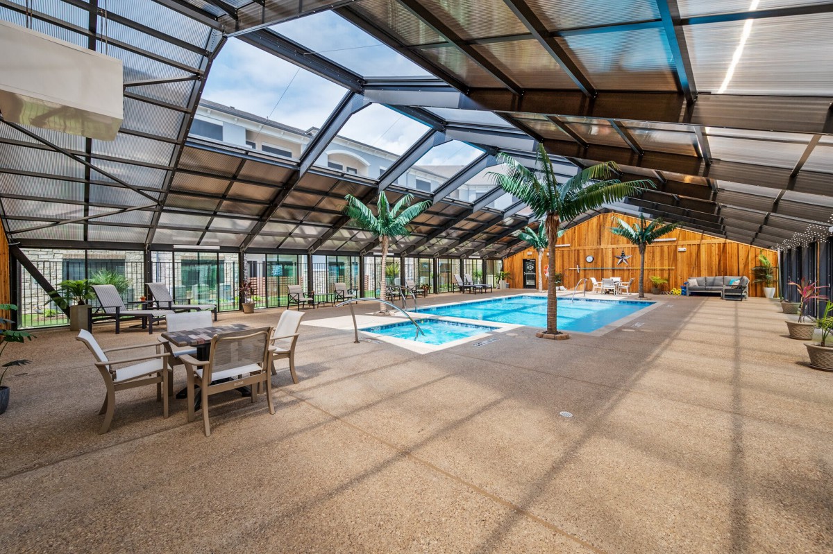 A spacious indoor swimming pool area with a glass ceiling, surrounded by palm trees and seating.