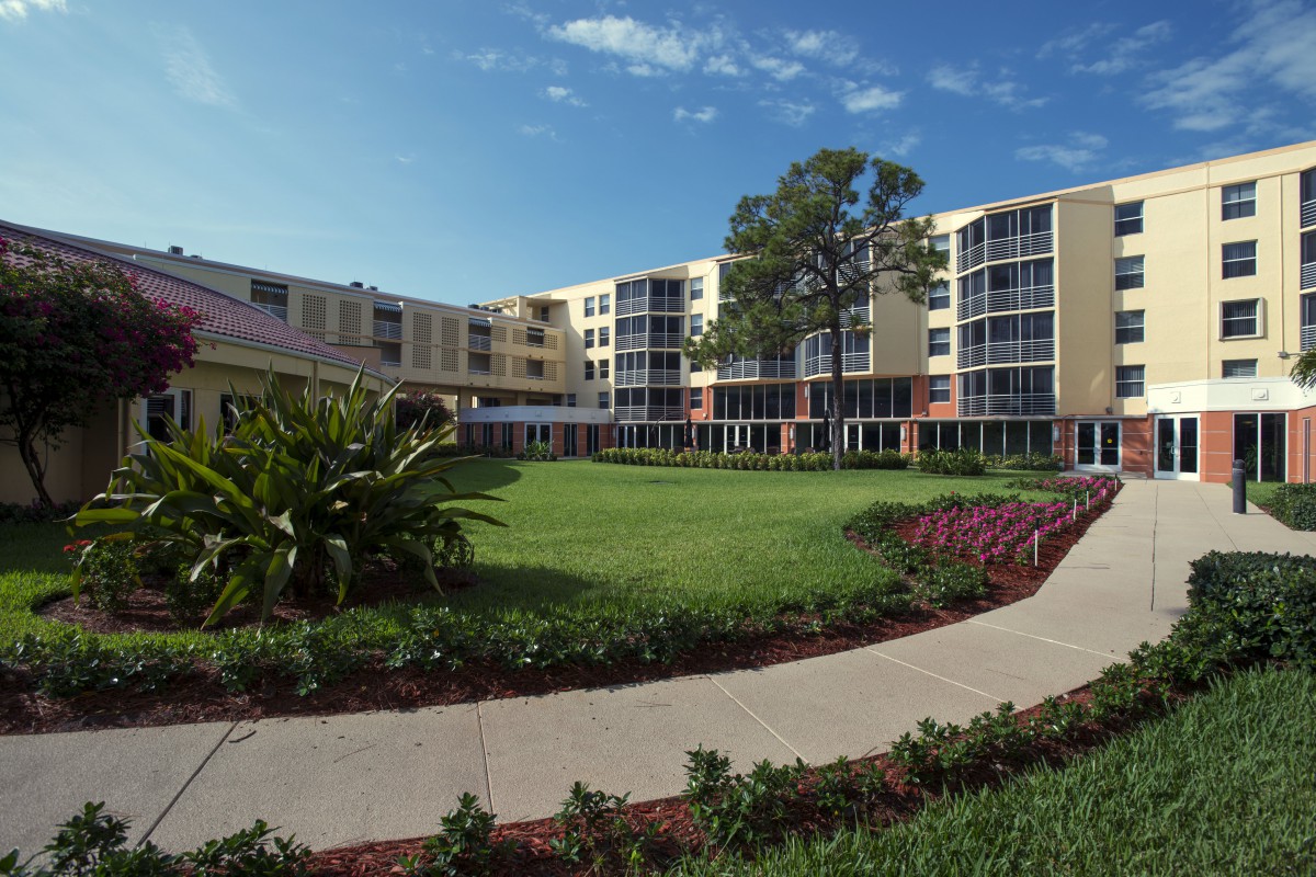 A college campus building surrounded by greenery and a clear blue sky.